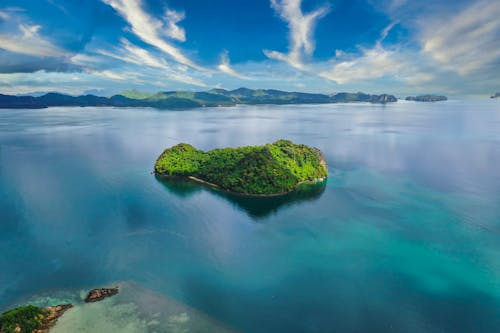 Green island in calm ocean water on sunny day