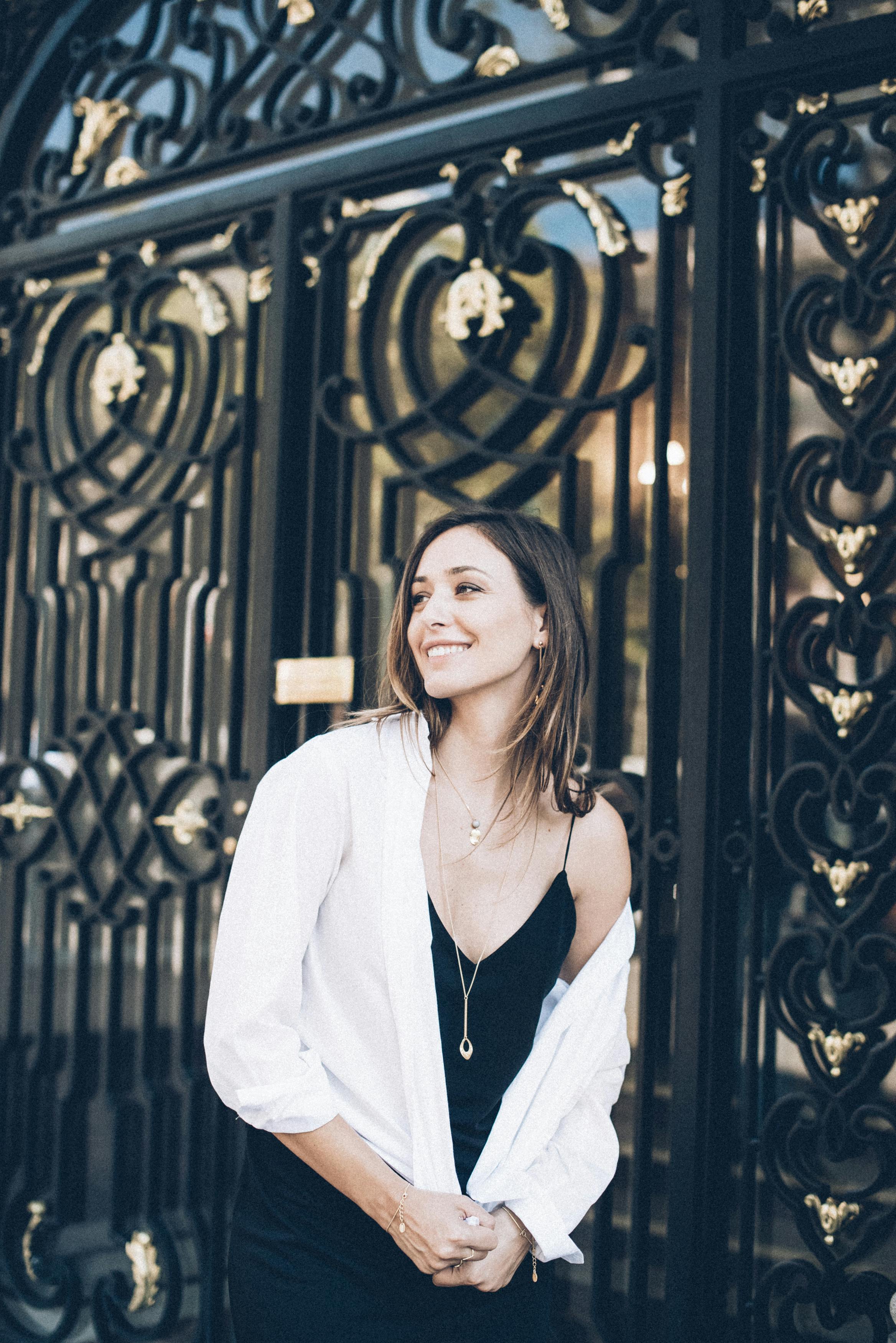 Free Elegant woman smiling in front of ornate black gate wearing a stylish black dress. Stock Photo