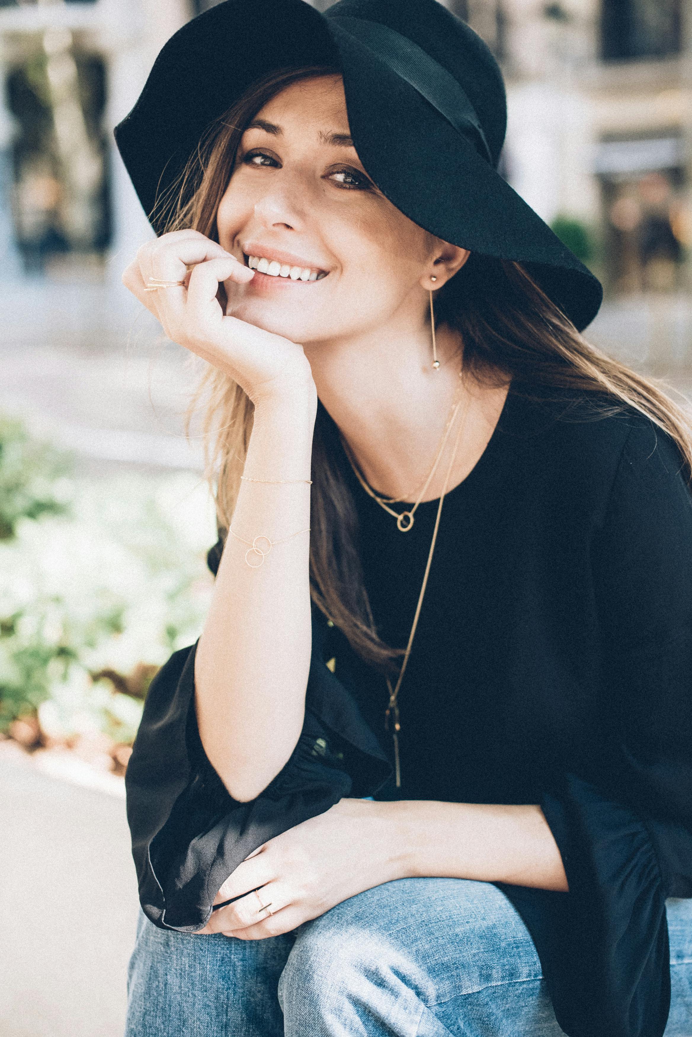 一位戴着黑色帽子和衬衫的迷人女性在户外微笑，尽显休闲优雅