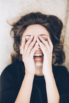 Joyful woman lying down, smiling with hands over face, wearing black top.