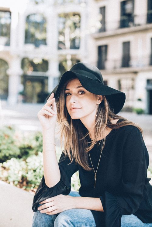 Free Casual portrait of a woman in fashionable attire sitting outdoors with a black hat. Stock Photo