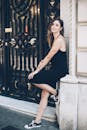 在城市环境中，一位穿着黑色连衣裙的时髦女人靠在装饰性大门上放松身心