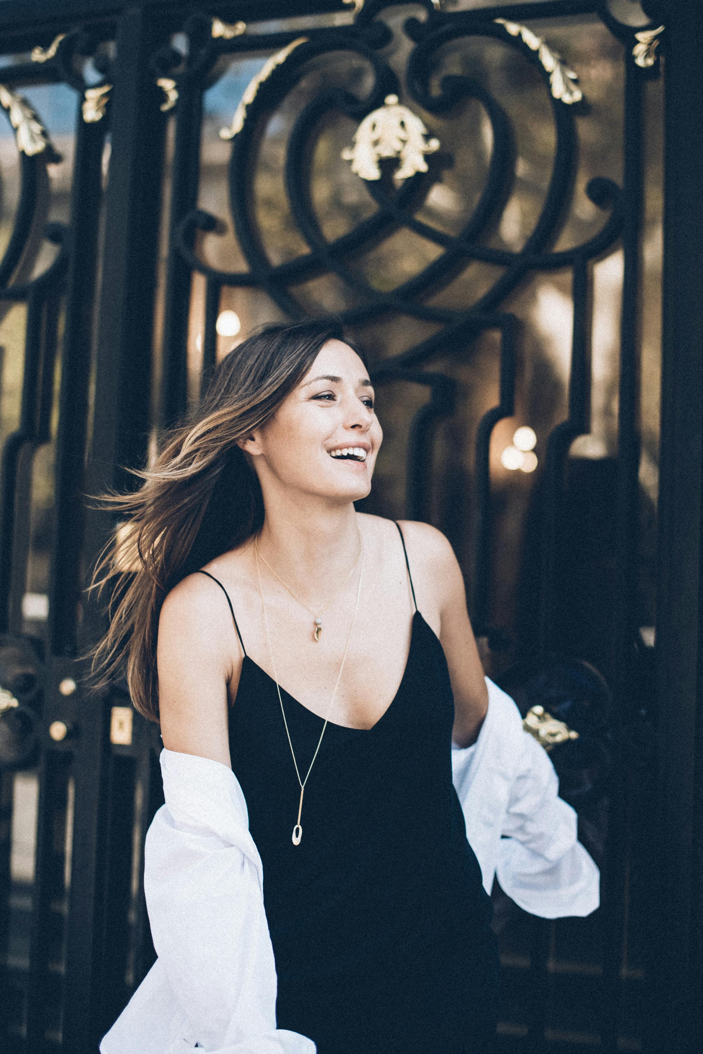 一位时尚女子身着优雅的黑色连衣裙，在户外微笑