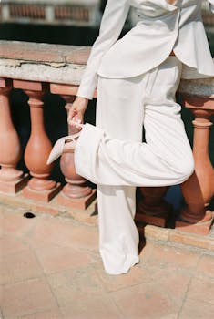 Chic fashion model in white suit posing with elegant heels on balcony. Stylish and contemporary look.