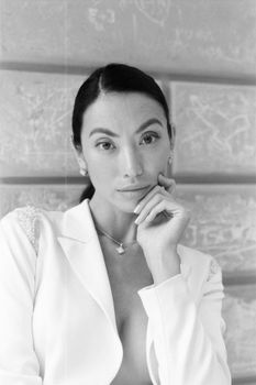 Black and white portrait of a woman in a white blazer against a concrete wall.