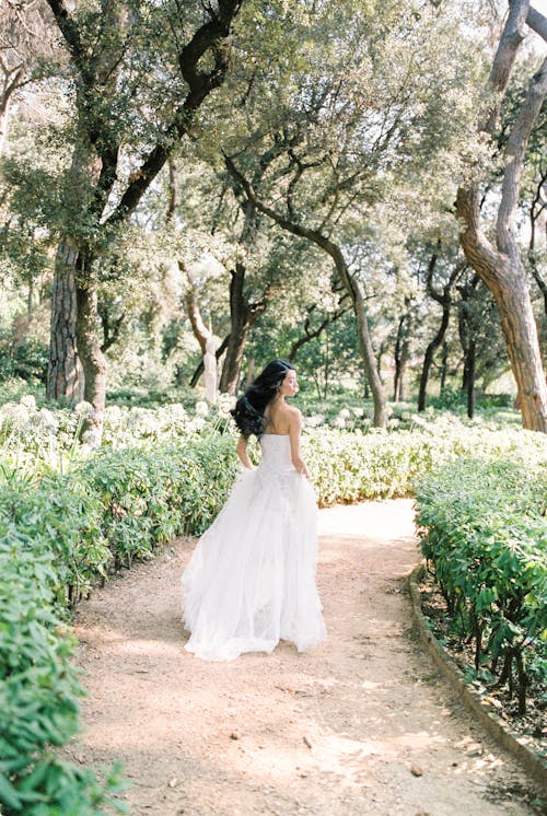 푸른 잔디와 나무 사이의 통로에 걷는 하얀 웨딩 드레스 여자