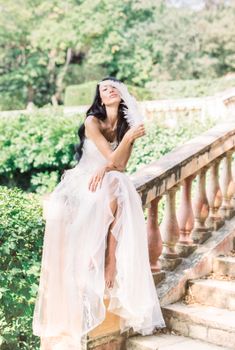 一位美丽的新娘穿着婚纱，优雅地坐在户外的石阶上，手里拿着一根羽毛