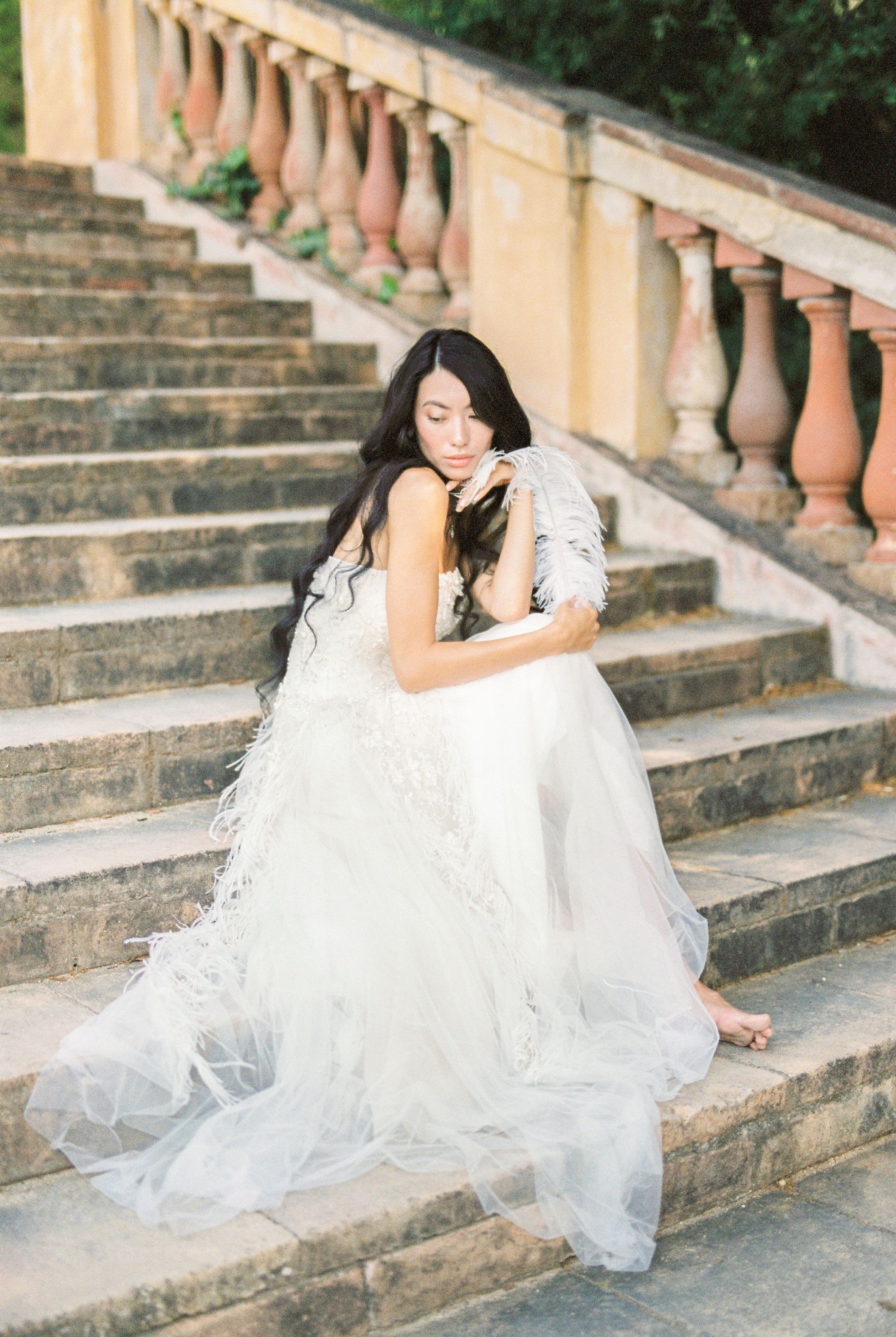 一位身穿羽毛婚纱的亚洲新娘，优雅地坐在古色古香的石阶上