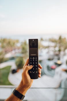 A person's hand holding a landline phone against a blurred outdoor scenic view.