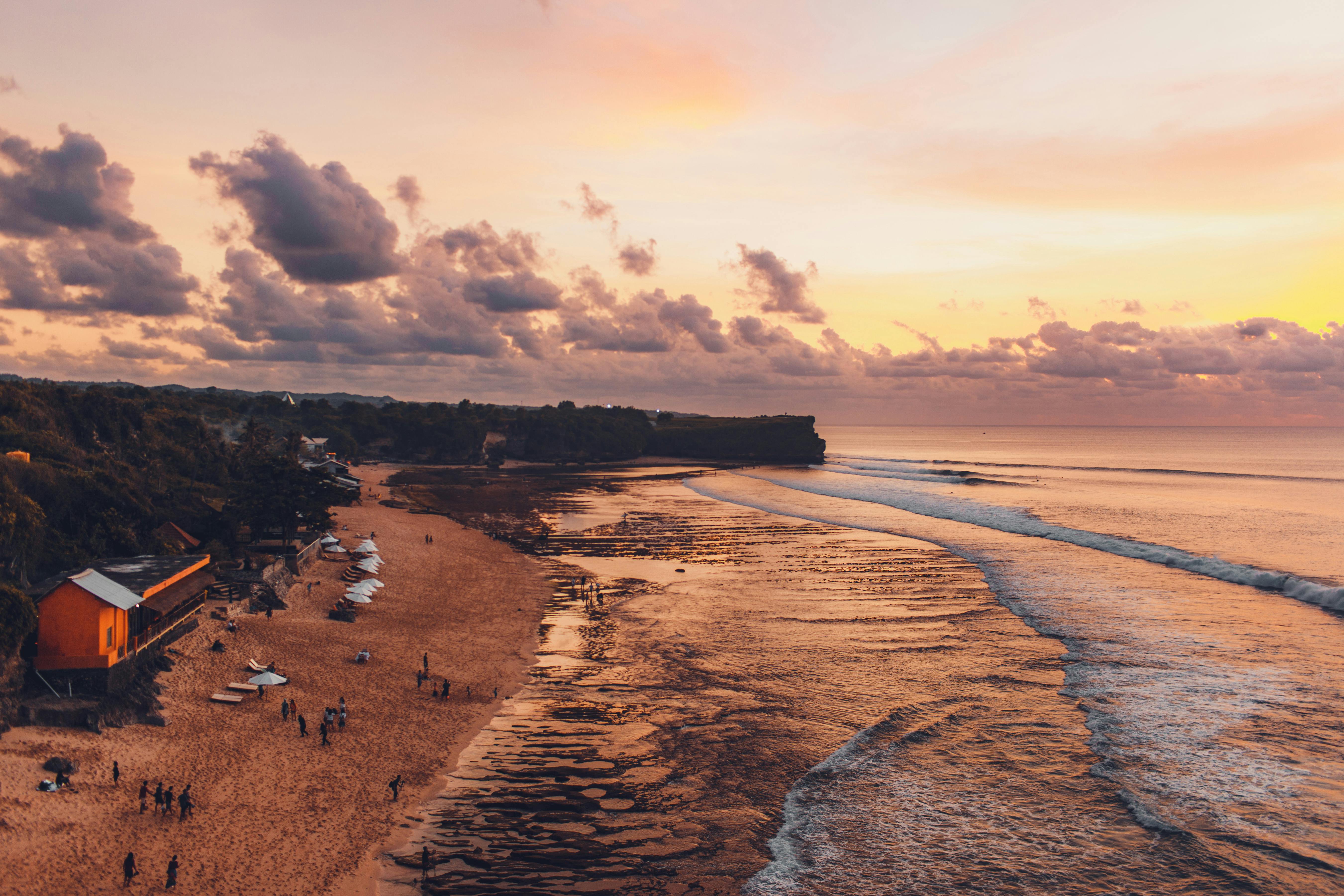 Calm reef-protected water at a Nusa Dua beach contrasted with a busy Seminyak beach club at sunset in Bali