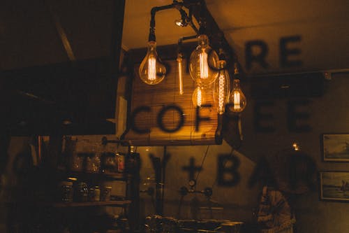 Through bar window view of glowing light bulbs in dark interior with cafeteria information on glass
