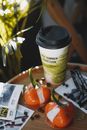 Top view of paper cup of coffee near pair of mousse cakes in colorful mirror glaze and coffee beans with cards on round table in cafeteria