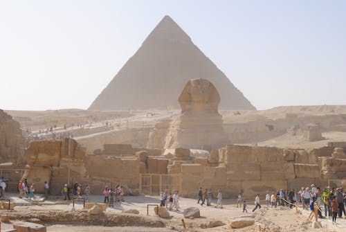 Unrecognizable distant travelers walking on old path near ancient Sphinx statue and Great Pyramid of Giza located in Egypt on sunny day