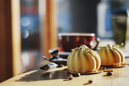 Delectable mousse cakes covered with velour on cardboard boards near coffee beans and sugar bags on wooden table in cafeteria in sunlight