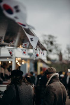 Bustling Korean street food market with people and flags, capturing lively urban atmosphere.
