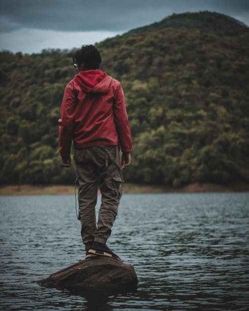 Anonymous tourist admiring nature while standing on stone in lake