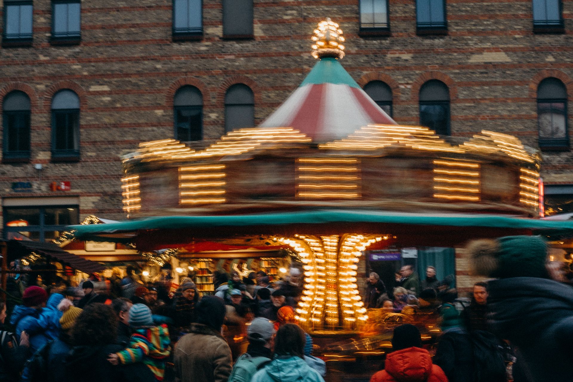 A carousel spins with bright lights at a bustling outdoor winter market festival.