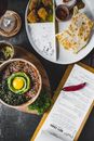 Top view of miso bowl with egg placed on table near menu and plate with various sauces and garnishes in exotic restaurant