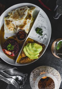 Top view of plate with red rice and roti bread served with sauces and avocado in cozy restaurant