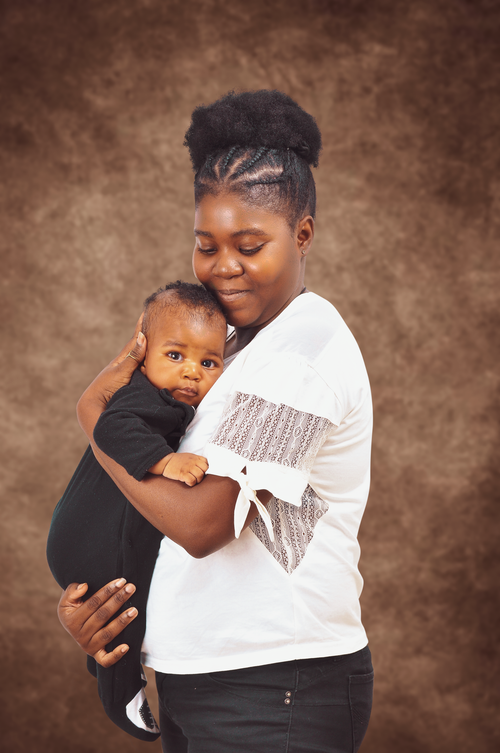 Free Side view of happy African American woman in casual clothes hugging adorable baby against brown background Stock Photo