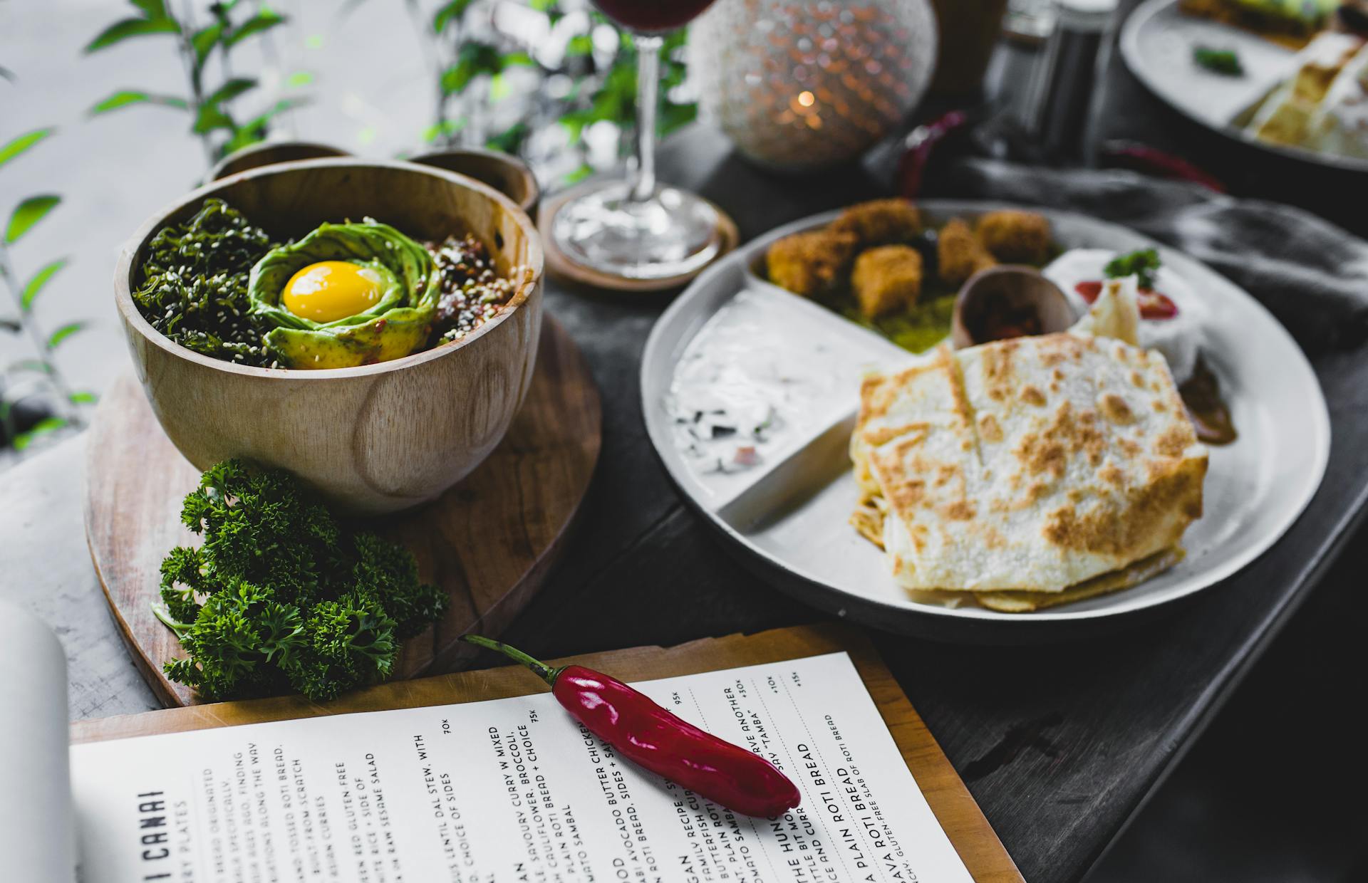 High angle of plate with roti bread and different Asian snacks placed on table with bowl of exotic food served with eggplant and avocado