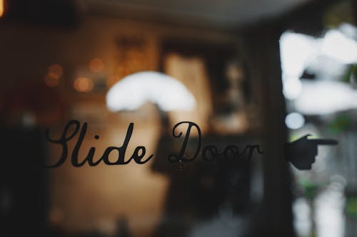 Slide door inscription on glass entrance of modern cafe against blurred interior during daytime