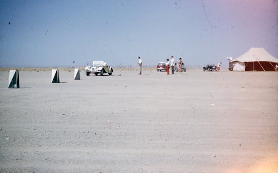 Vintage cars with people in a sparse desert landscape under a clear sky.