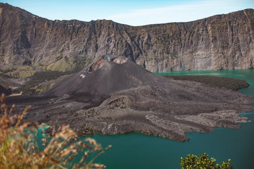 Magnificent view of majestic Rinjani volcano located on crater lake with crystal clean blue water and surrounded with rocky cliffs on clear day