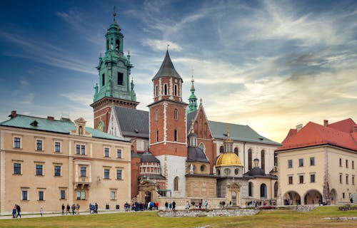 Traditional aged buildings and ancient Wawel Cathedral with various towers located on hill in Krakow against cloudy blue sky at sunset