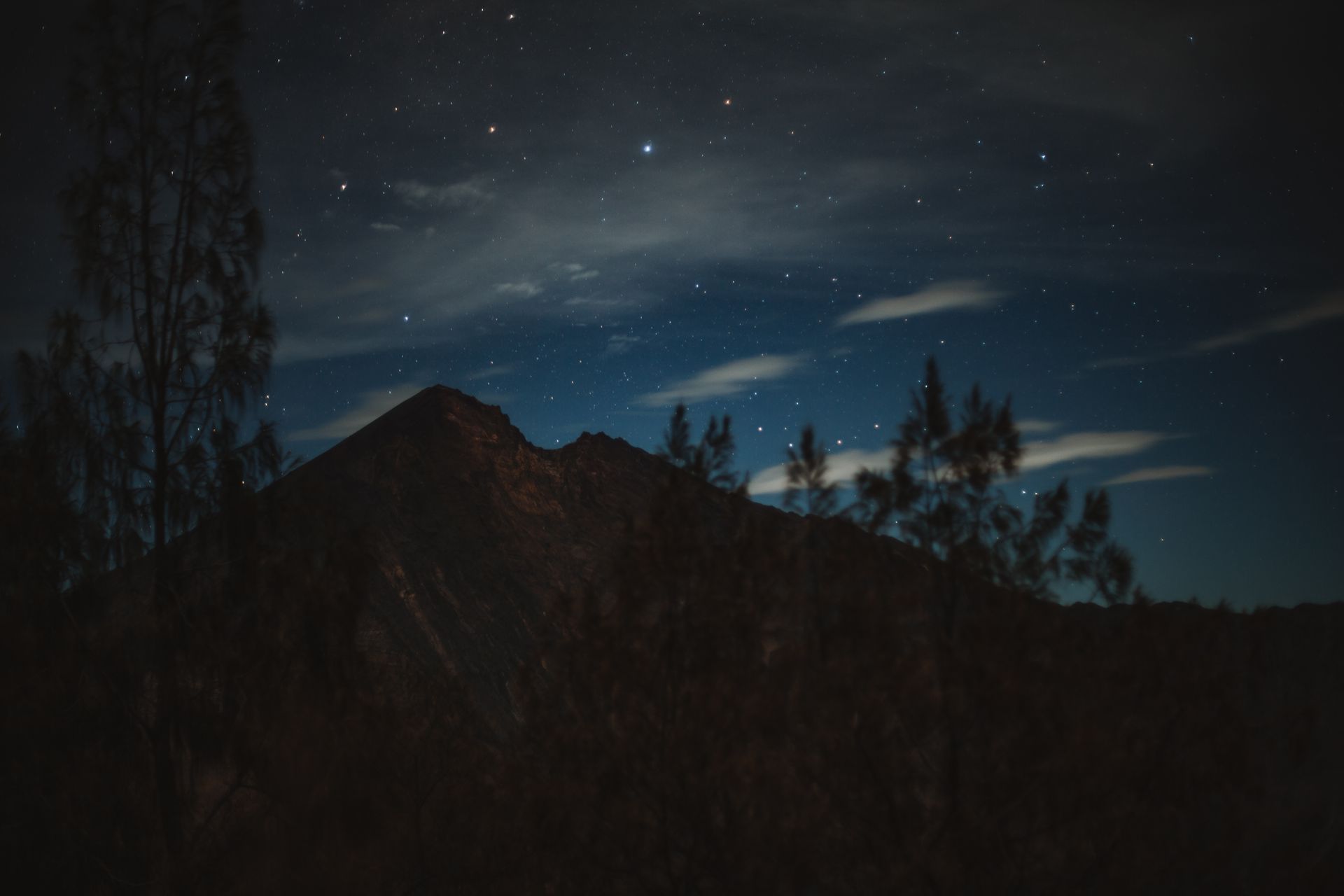 Dramatic silhouette of distant mountain summit located against cloudy dark sky during starry quiet night