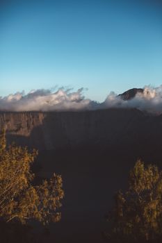 背景是岩石悬崖和山峰，云和蓝天，前景有树木