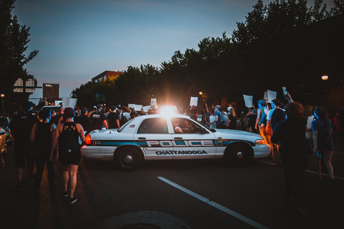 Police car with lamp on roof among group of protesters with posters and banners at night