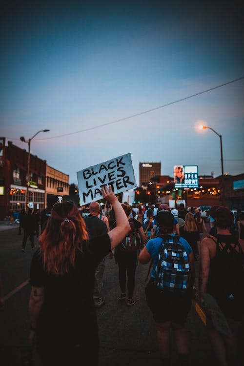 Back view of group of demonstrators showing banners with slogans in downtown under dark blue sky at night