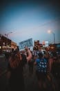 Back view of group of demonstrators showing banners with slogans in downtown under dark blue sky at night