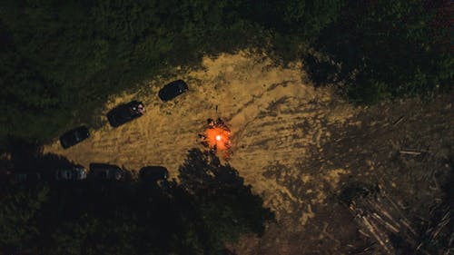 Free Drone view of group of friends chilling in campground around fire surrounded by forest at night Stock Photo