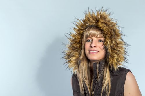 Free Studio portrait of a smiling woman in a fur-lined hooded vest against a blue background. Stock Photo