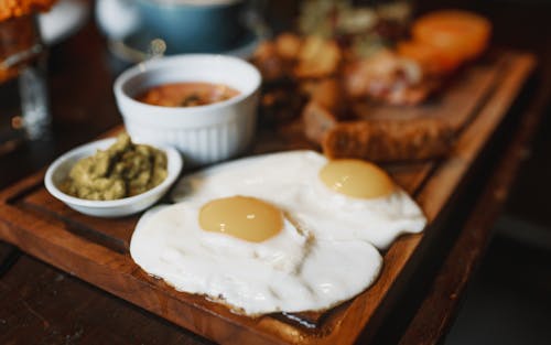 Free Satisfying breakfast of tasty fried eggs and different delicious appetizers served on wooden stand on table Stock Photo