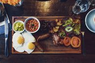 Top view of delicious fried eggs and vegetables with sausages and beans on wooden tray with fork and knife
