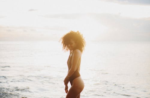 Free Side view of smiling woman with curly hair in swimwear standing in sea and enjoying sunset while spending weekend outside Stock Photo