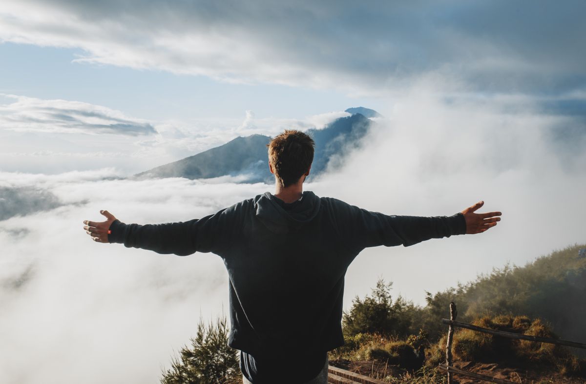Person standing on a mountain with arms outstretched, looking out over a vast landscape with a sense of freedom and hope
