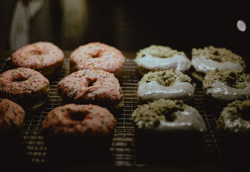 Assortment of pink and white glazed donuts with sprinkles on a metal rack.