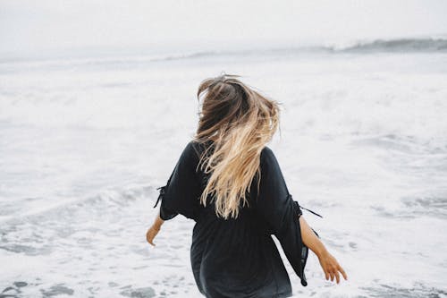 Anonymous woman walking near waving sea