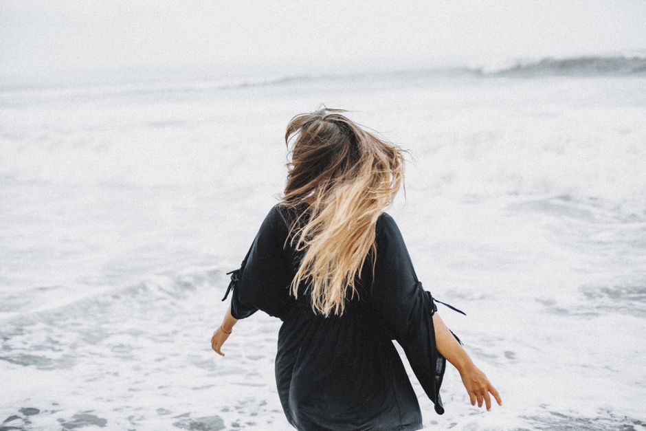 Back view of unrecognizable female in casual clothes standing near stormy sea waves