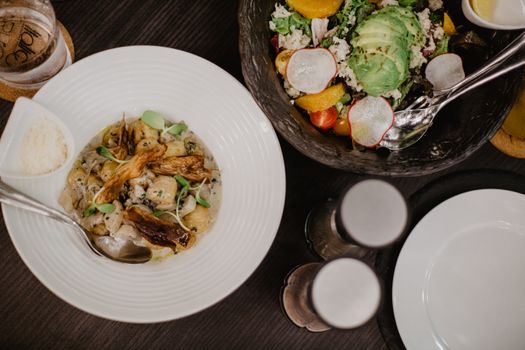 Top view of plate with stewed vegetables and meat placed on black table near bowl with fresh salad and jars with spices
