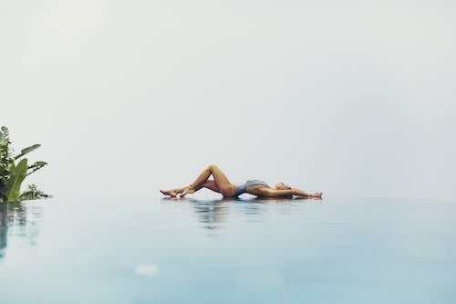 Free Side view of barefoot young lady in swimsuit lying on poolside and reflected in water while resting on resort Stock Photo