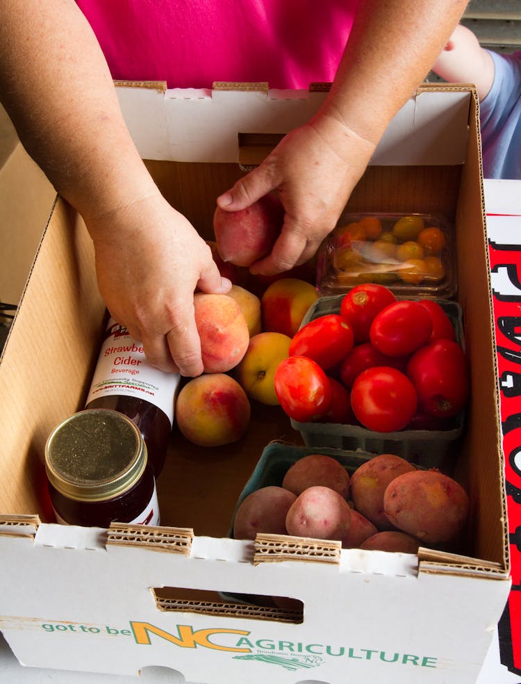 Hands Arranging Fruits And Vegetables In Brown Cardboard Box