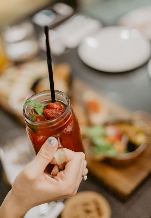 Free From above of anonymous female holding glass cup of red beverage with straw decorated with strawberries and mint leaves in cafe Stock Photo