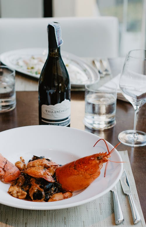 From above of plate with delicious dish from lobster served with bottle of wine placed on wooden table near glass of water and wineglass in restaurant