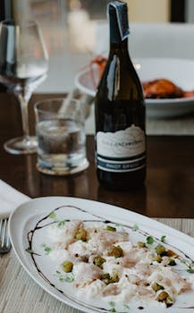 Gourmet appetizer from fish with sauce and green olives served on plate placed on wooden table with bottle of wine in restaurant