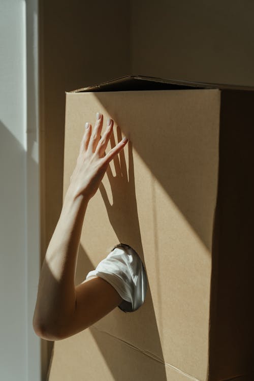 Free Person in White Shirt and Blue Denim Jeans Sitting on Brown Cardboard Box Stock Photo